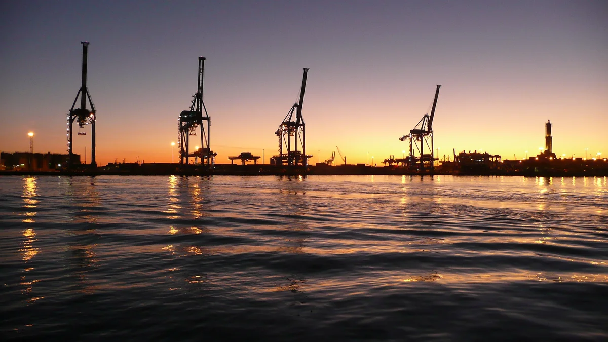 Le gru del porto di Genova e la Lanterna al tramonto, viste dal mare