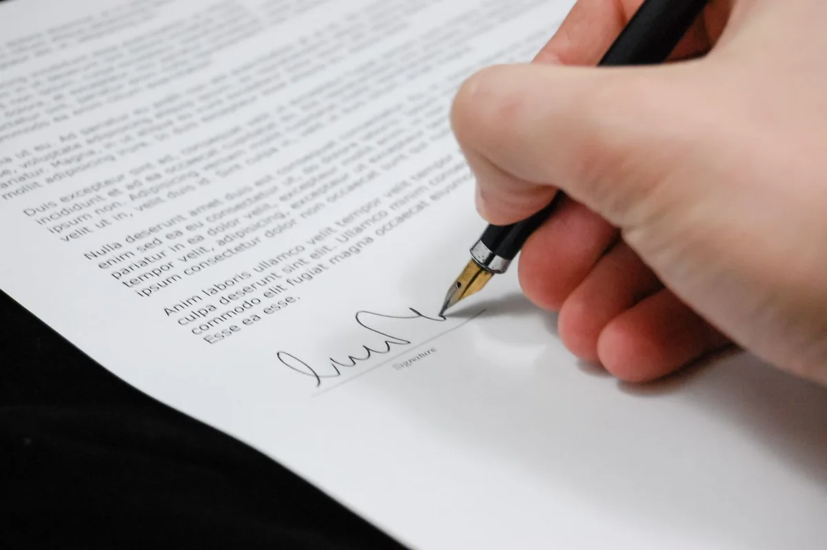 Mano che firma un contratto assicurativo con le clausole in primo piano