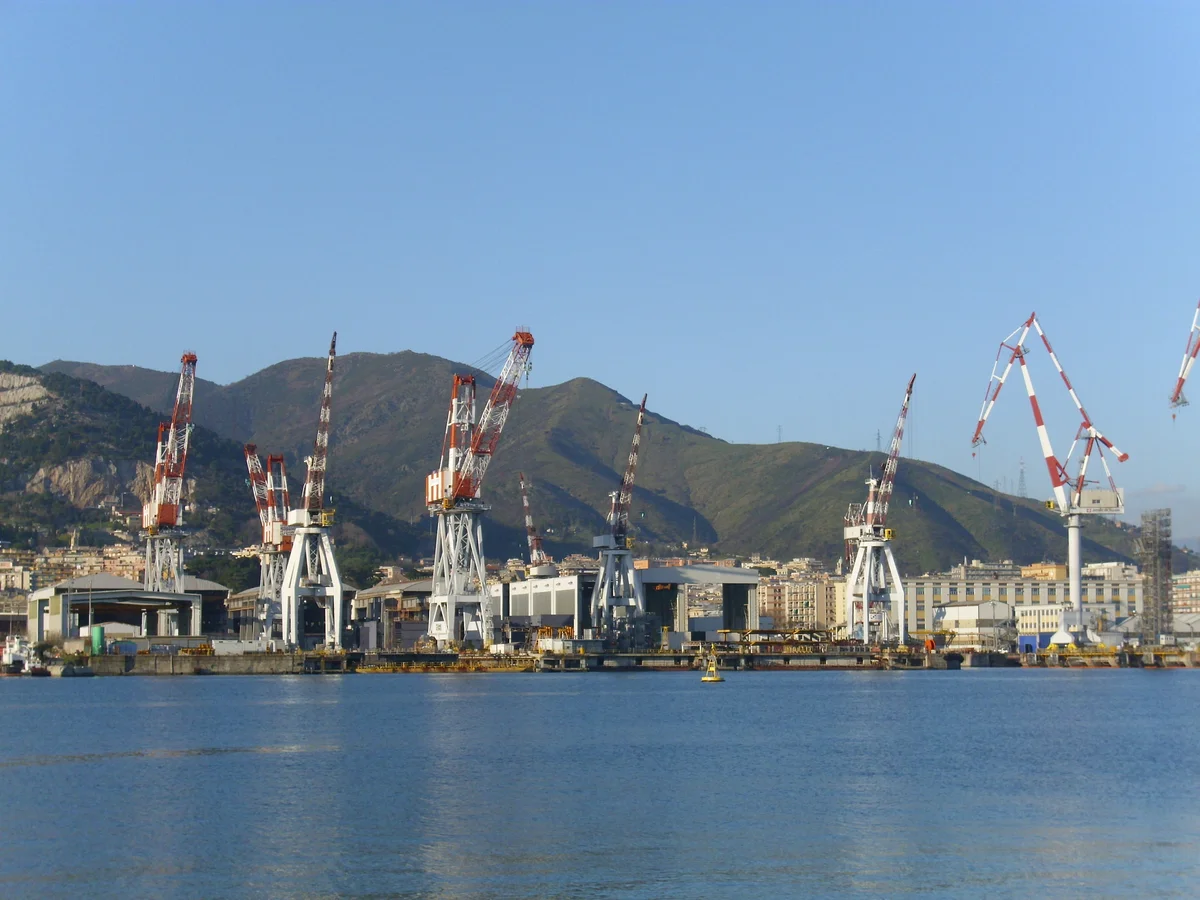 Le gru rosse e bianche del cantiere navale di Sestri Ponente viste dal mare, con le alture di Genova alle spalle